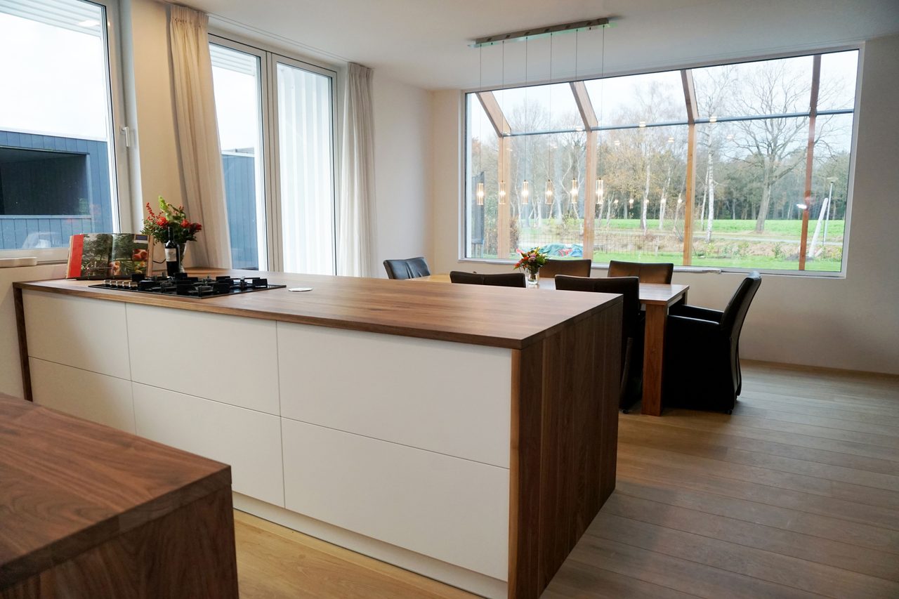 Witte keuken met een houten werkblad en een kookeiland, met uitzicht op de tuin